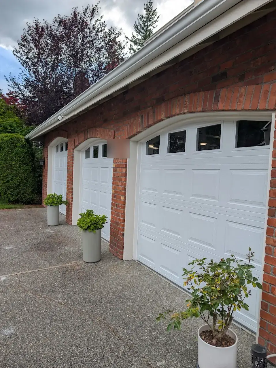 Same Bellevue brick home with three new white garage doors after installation
